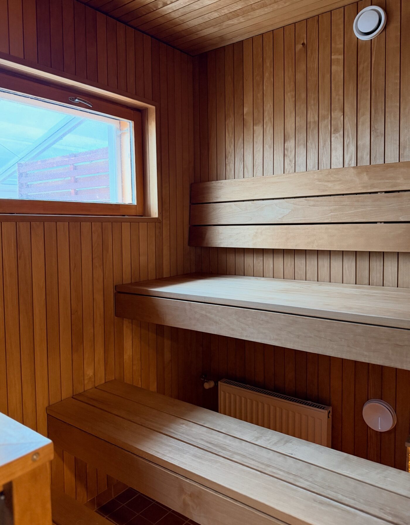 Remaconin saneeraama sauna, jossa puuverhoillut seinät, leveät lauteet ja ikkuna